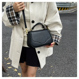 Détail du sac de selle en cuir noir avec rabat ondulé et finitions métalliques dorées