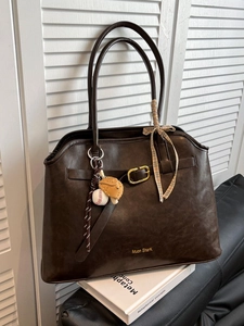 Sac fourre-tout rétro marron foncé en cuir avec ruban et charm baseball sur canapé noir
