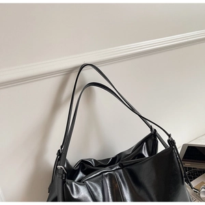 Detail of glossy black PU leather tote with silver buckle and refined pleat texture