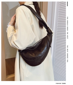 Detail of dark brown leather crescent bag featuring a knotted strap on model shoulder