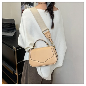 Détail du sac selle beige en similicuir avec large bandoulière tissée porté à l'épaule