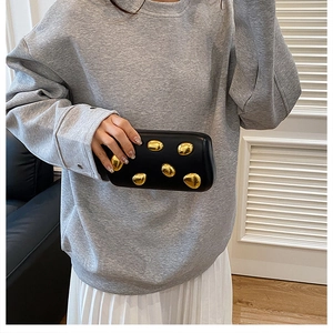 Modella che indossa una pochette nera da sera con ovali dorati e tracolla a catena