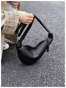 Close-up of black croissant bag with knotted shoulder strap and metal zip detail