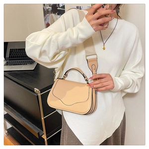 Détail du sac de selle en cuir beige avec rabat ondulé et bandoulière en toile