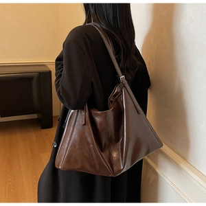 Detail of dark brown leather tote bag showing shiny texture and adjustable strap buckle