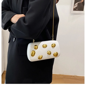 Dettaglio laterale della pochette bianca a scatola con decori dorati e catena