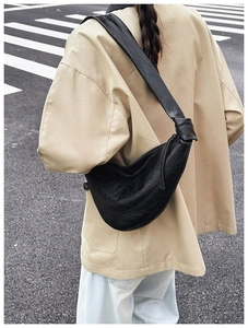 Close-up of black leather half-moon crossbody bag with decorative shoulder strap knot