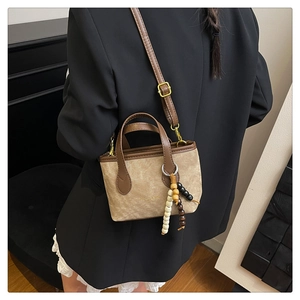 Detail of khaki suede bucket bag with wooden bead tassel shown in a lifestyle setting