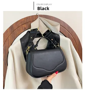 Détail d'un sac selle noir mat avec boucles dorées, poignée supérieure et bandoulière large