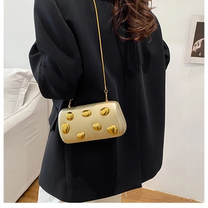 Clutch rigida color champagne con borchie 3D dorate e catena su un blazer nero