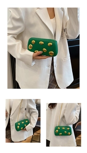 Dettaglio della pochette in pelle verde smeraldo con accenti metallici dorati e catena