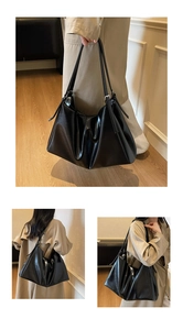Detailed view of a black pleated tote bag with glossy finish and long shoulder straps
