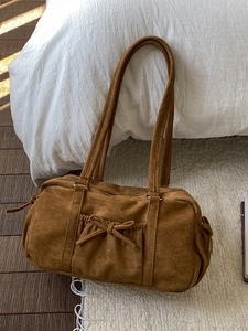 Sac à main en daim caramel avec nœud décoratif sur un tapis blanc moelleux