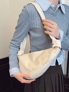 Minimalist beige leather crescent saddle bag with knot detail worn by a model