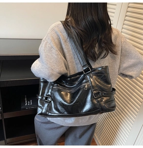Detail of black oil wax leather tote bag with logo embossing and side buckle straps