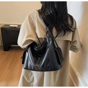 Detail of black leather tote bag with side flap pockets worn with a stylish trench coat