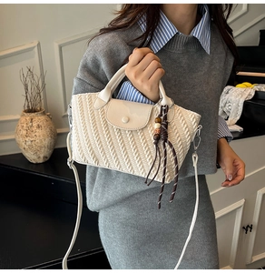 Close-up of cream woven texture shoulder bag with retro bead charm and leather handle