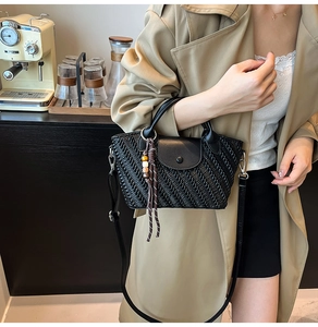 Close-up of black woven texture handbag with leather flap and beaded tassel detail