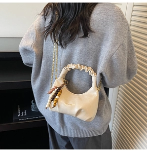 Detail of cream pleated crescent bag with gold chain and colorful bead pendant accessory