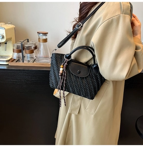 Detail of black woven crossbody bag with leather handles and bohemian bead charm