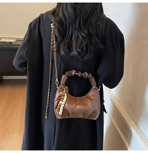 Detail of dark brown leather hobo bag with scrunchie handle and beaded pendant