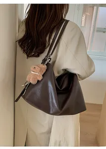 Detail view of large dark brown tote bag with cute plush bear charm on a trench coat