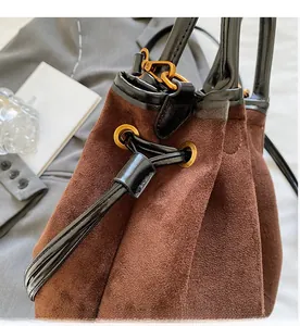 Detail of brown suede bucket bag featuring drawstring opening and black leather trim