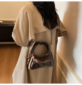 Detail of coffee brown pleated cloud bag with wooden bead charm and chain strap
