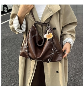 Detail of dark brown leather tote bag with contrast stitching and baseball charm decor
