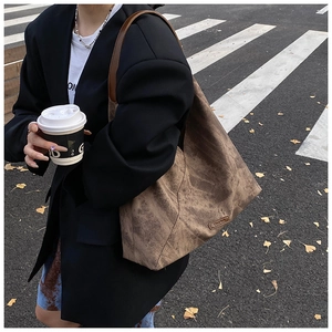 Detail of vintage brown suede tote bag with leather strap and debossed logo on street background