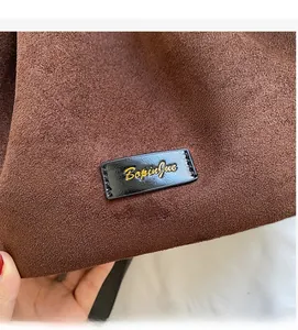 Detailed close-up of dark brown suede bucket bag with leather brand tag and gold lettering
