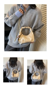 Detail of cream pleated dumpling bag with gold chain strap and beaded charm on model