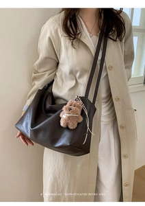 Detail of dark brown leather tote bag with plush bear charm worn with a light trench coat