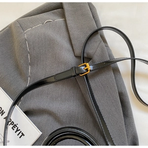 Close-up of sleek black patent leather belt with a gold buckle on a grey suit