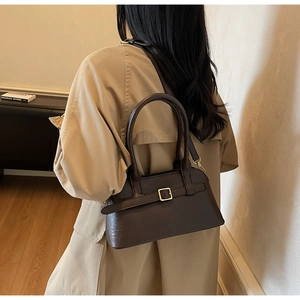 Detail of minimalist dark brown leather shoulder bag on a model wearing a classic trench coat
