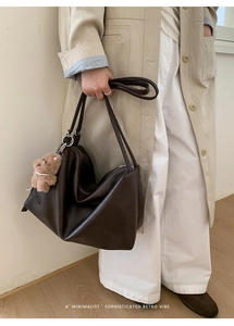 Detail of dark brown leather tote bag featuring a cute plush bear charm on the strap