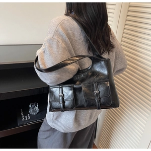 Detail of vintage black glossy leather tote bag with double buckle pockets on shoulder