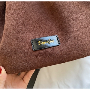 Detail of dark brown suede bucket bag featuring black leather logo tag with gold embossing