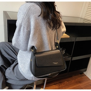 Detail of black crossbody bag with woven flap and gold fashion logo shown on model