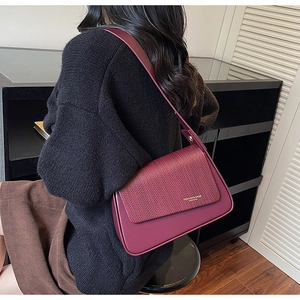 Detail of burgundy shoulder bag featuring woven texture flap and gold fashion lettering