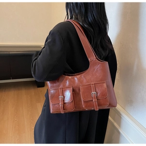 Detail of reddish brown shoulder bag featuring dual front pockets with silver buckles