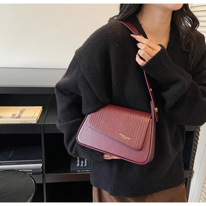 Detail of dark red crossbody bag with woven texture lid and wide strap in lifestyle setting
