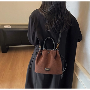 Detail of dark brown faux suede bucket bag with drawstring and black handle on model