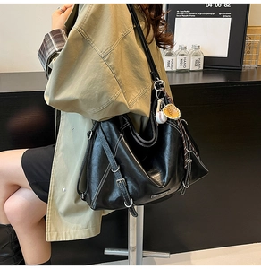 Detail of black tote bag with white stitching and baseball charm on a trench coat