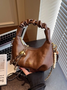 Brown leather crescent bag with ruched handle and gold chain strap in aesthetic setting