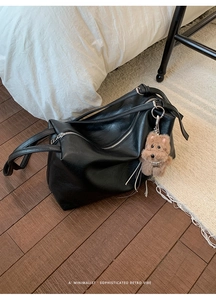 Close-up of black PU leather tote bag with silver zipper and brown plush bear charm