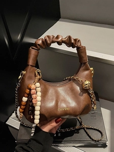 Dark brown pleated cloud handbag with beaded charm and chain strap in a stylish studio setting