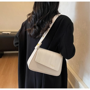 Model wearing a cream-colored crossbody bag with a woven leather texture and wide strap