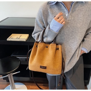 Detail of faux suede bucket bag featuring drawstring closure and leather handle trim