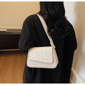 Detailed view of a white shoulder bag with woven texture and a wide strap on a model